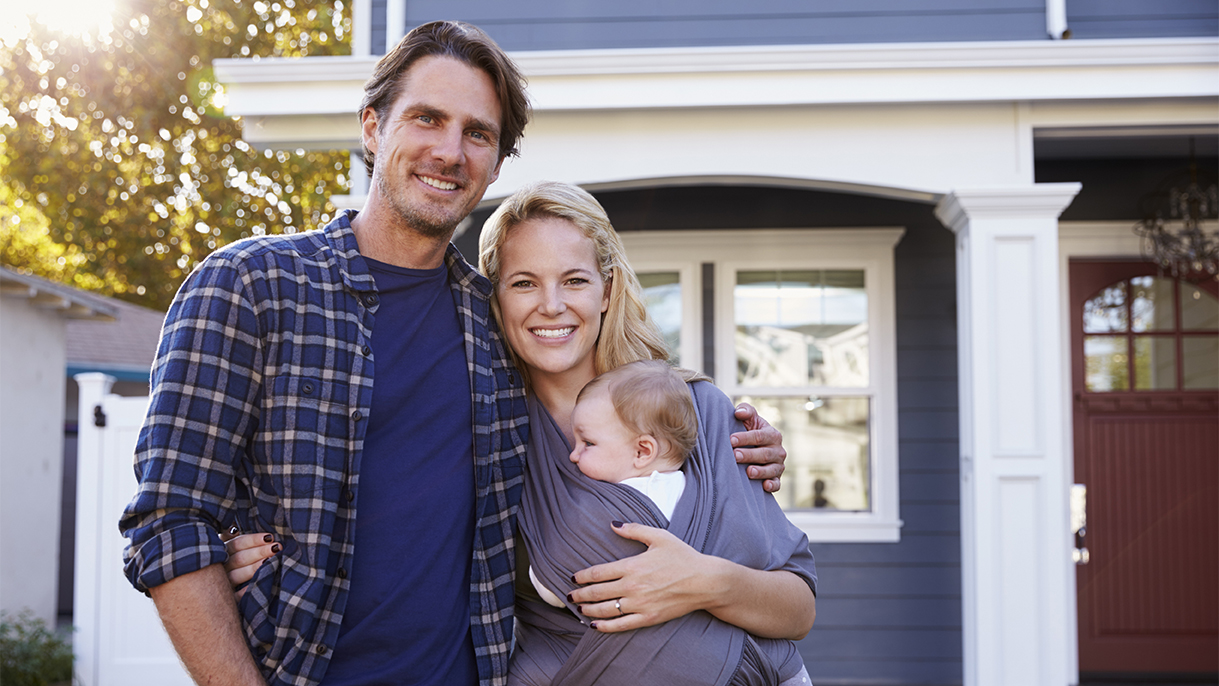couple with baby standing in front of house